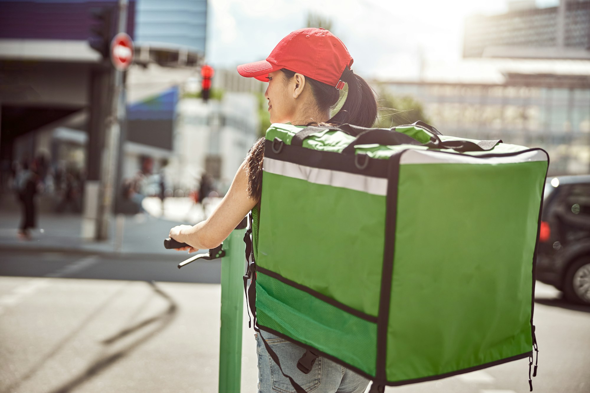 Food courier on scooter carrying food delivery bag through city